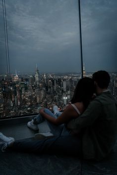 a man and woman sitting on top of a tall building looking at the city below