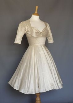 a white dress on a mannequin stand with a gray wall in the background