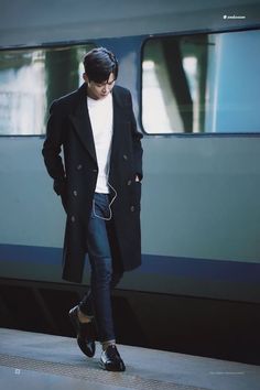 a man in black coat and headphones walking on train platform