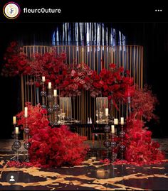 red flowers and candles are on display in front of a black backdrop with gold bars