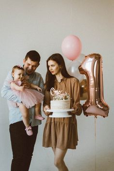 a man and woman holding a baby while standing next to a cake