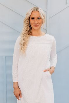 a woman wearing a white dress and smiling at the camera with her hands in her pockets