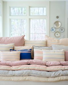 a bed with many pillows on it in front of two windows and plates hanging on the wall