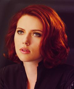 a woman with red hair and blue eyes looks into the distance while wearing a black shirt