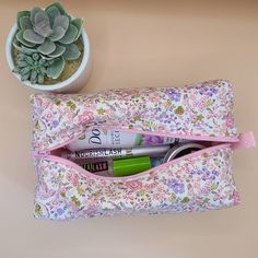 a pink flowered pouch with some pens and pencils in it next to a succulent plant