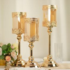 two gold candlesticks sitting on top of a table next to plates and flowers