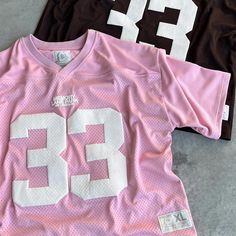 three pink and black football jerseys are laying on the ground, one has white numbers