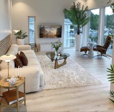 a living room filled with lots of furniture and plants on top of a wooden floor