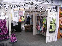 an outdoor market with clothes on display and cow print fabric hanging from the top of it