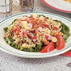 a white plate topped with pasta salad next to a glass of water and silverware