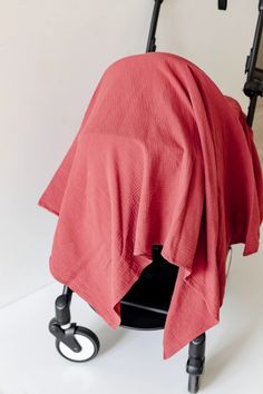 a chair covered with a red blanket on it's back and wheels in front of a white wall