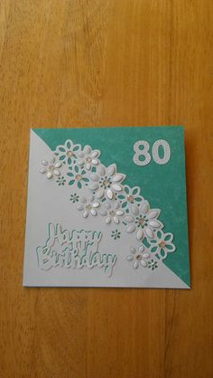 an 80th birthday card with white flowers and green paper on a wooden table top