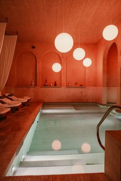 an indoor swimming pool with lights hanging from it's ceiling and chairs in the background