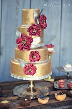 a three tiered wedding cake with red flowers on the top and gold icing