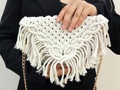 a woman holding a white crocheted purse with chains around her neck and hands on the shoulder