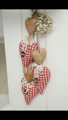 three wooden hearts hanging from the side of a white wall with flowers in them and two other heart shaped ornaments attached to it