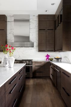 a kitchen with wooden cabinets and white marble counter tops, along with flowers in vases