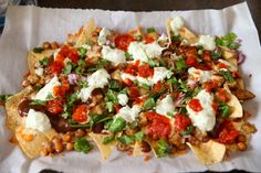 nachos topped with beans, cheese and tomatoes on top of a white napkin