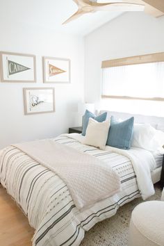 a white bed sitting in a bedroom next to a wooden dresser and window with pictures on the wall