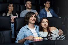 three people sitting in a movie theater and one is holding a popcorn cup while the other looks on