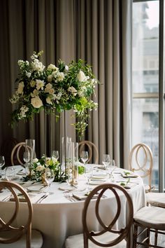 the table is set with white flowers and greenery in tall vases on top