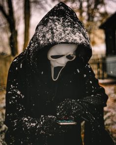 a person wearing a mask and holding a cell phone in their hands while standing in the snow