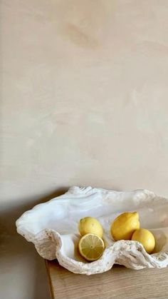 a white bowl filled with lemons on top of a wooden table next to a wall