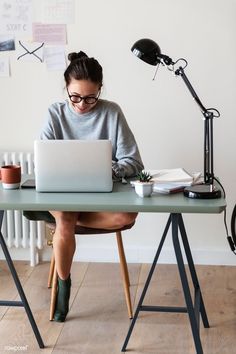 a woman sitting at a desk with a laptop computer and lamp on top of it