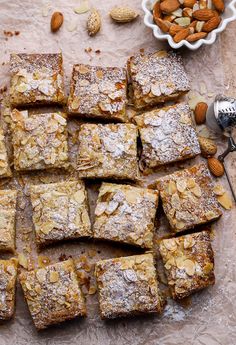 almond bars are arranged on a piece of parchment paper next to a bowl of nuts