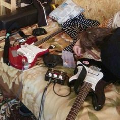 a woman laying on top of a bed next to two electric guitars and an amp