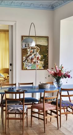 a dining room table with blue chairs and a painting on the wall behind it,