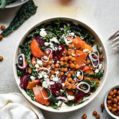 a white bowl filled with vegetables and chickpeas next to silverware on a table