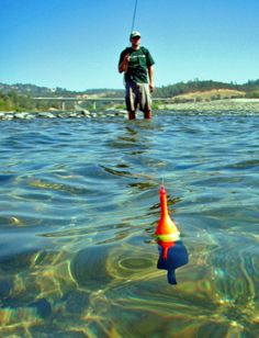 a man standing in the water holding a fishing rod and an orange cone shaped object