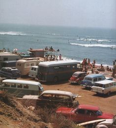 many cars and buses are parked on the beach near the ocean as people swim in the water