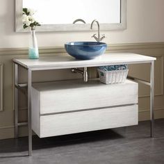 a bathroom vanity with a blue bowl on the sink and a mirror above it, in front of a white wall