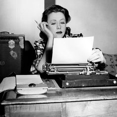 a woman sitting at a desk with an old typewriter in front of her face