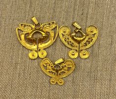 two gold colored metal pieces with designs on them, sitting on a cloth covered surface