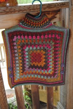 a crocheted granny blanket hanging from a wooden porch rail with flowers in the background