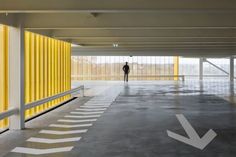 a man standing in an empty parking garage next to yellow and white striped walls with arrows painted on the floor