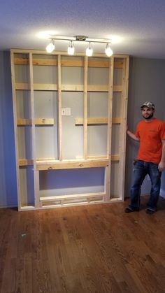 a man standing in front of a bookcase made out of plywood planks