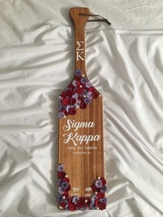 a wooden sign with flowers hanging from it's side on a white bed sheet