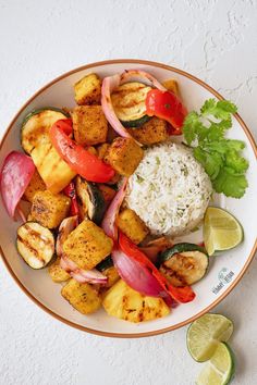 a white plate topped with vegetables and rice next to lime wedges on a table