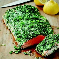 a piece of salmon covered in pesto next to a knife on a cutting board