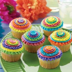 cupcakes decorated with brightly colored icing on a green plate next to flowers