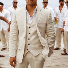 a man in a suit standing on a dock with other men behind him wearing white shirts and tan pants