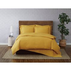 a bed with yellow sheets and pillows in a room next to a potted plant