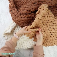 a woman is knitting a crocheted blanket on the floor with her hands and fingers