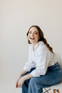 a woman sitting on top of a white chair with her legs crossed and smiling at the camera