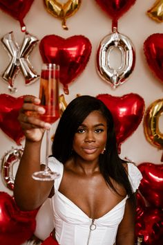 a woman holding a wine glass in front of red and gold foil heart shaped balloons