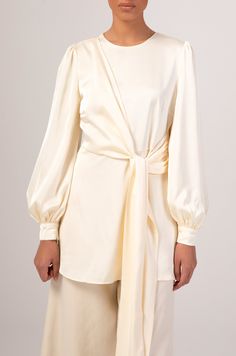 The Hala blouse features an extravagant side wrap with self fabric belt, oversized balloon sleeves and a rich satin fabric. Model is 5'7/US 02 and wears a size XS. Cream Silk Blouse For Evening, Silk Cream Evening Blouse, Cream Silk Evening Blouse, Chic Satin Wrap Blouse, Elegant Wrap Top For Brunch, Silk Wrap Blouse For Evening, Silk Evening Wrap Blouse, Evening Blouse With Gathered Sleeves In Satin, Cream Satin Long Sleeve Blouse